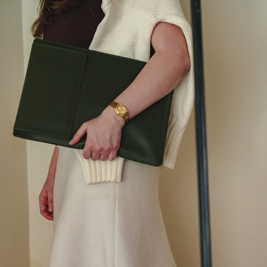 Person holding a green laptop sleeve wearing a white dress.